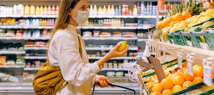 woman with a face mask holding lemon in a supermarket